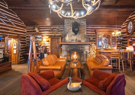 Room in a cabin with leather chairs and a stone fireplace in the center