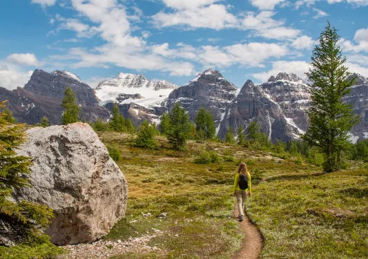 Woman walking along a dirt trail with large mountains in the distance