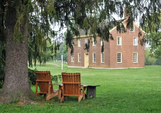 Two wooden chairs on a grass field, with a brick building in the background
