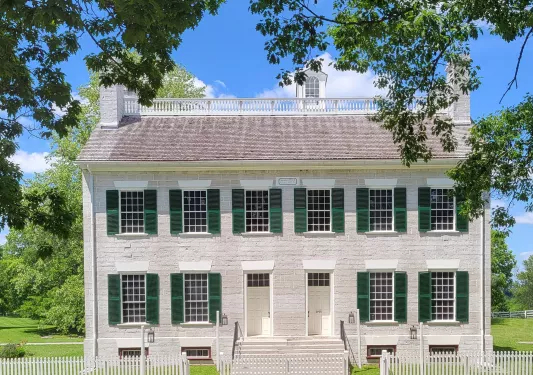 White brick building with large grass field and tall trees in the background
