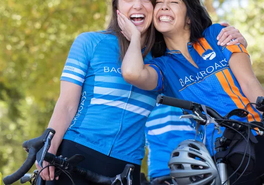Two women smiling while standing on top of their bicycles
