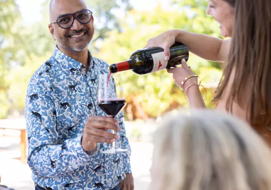 Man smiling, holding up a glass while a woman pours wine into the glass