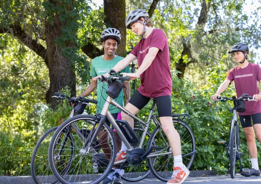Two boys smiling while standing next to electric bicycles