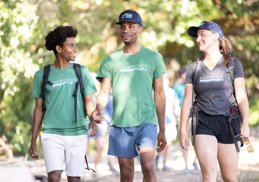 Two men and one woman walking on a trail with blurry trees in the background