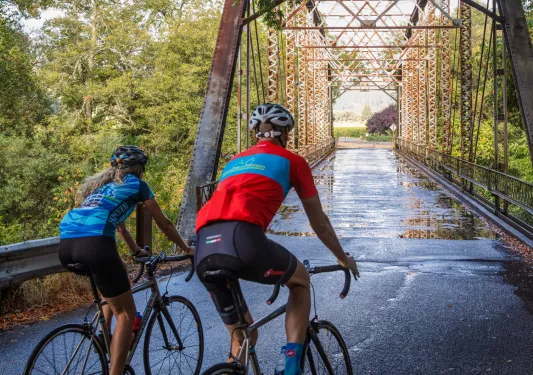 Man and woman biking on a bridge that is covered in puddles