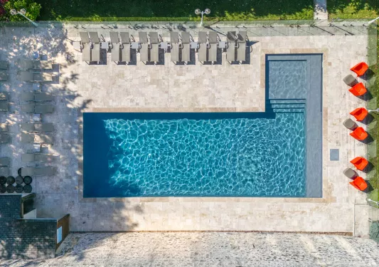 Sky view of an outdoor pool, surrounded by reclining chairs and grass fields