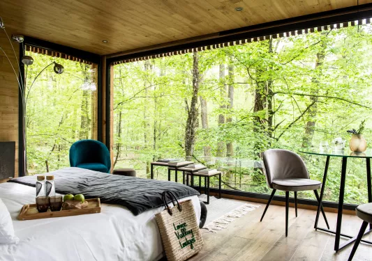 Bedroom with large windows looking our to a forest, with a wooden tray on top of the bed