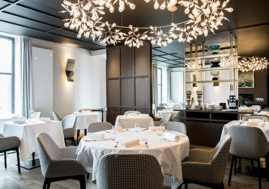 Hotel dining area with checkered chairs and circular white tables, with large light fixtures above