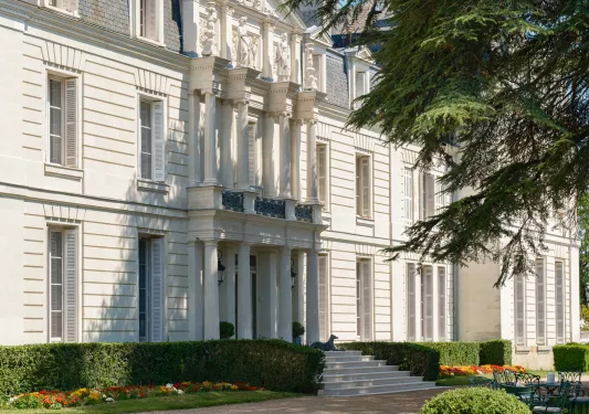 Exterior view of a white, stone building with large pillars and trimmed bushes