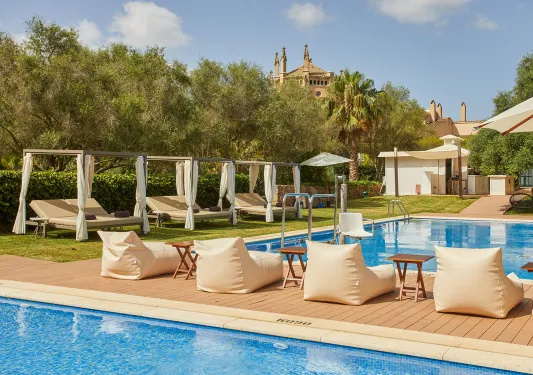 Outdoor pool with cushioned, reclining chairs and trees surrounding