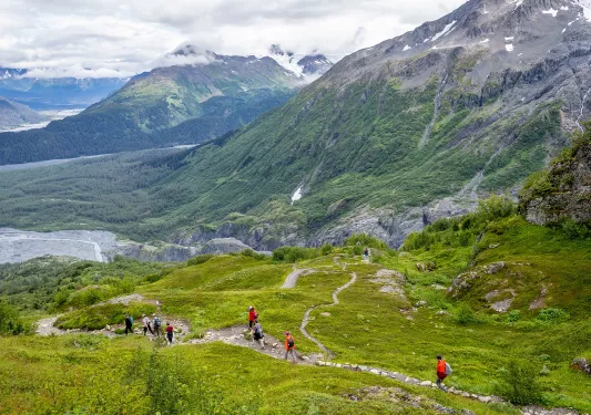 Group of people walking through a grassy trail with large mountains in the distance