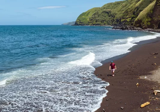 Man walking on a beach, with grassy mountains in the background