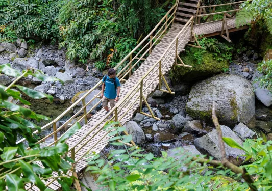 Man walking on a wooden bridge over a small river full of boulders