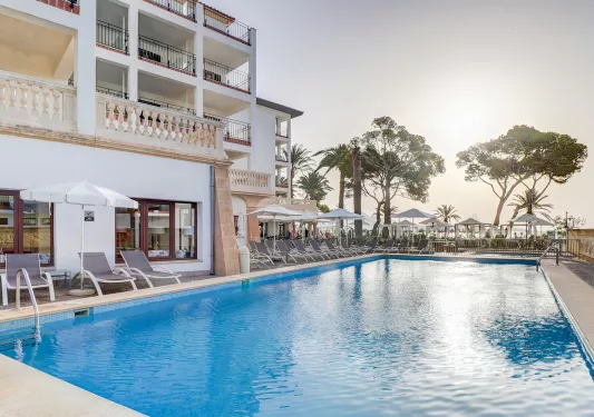 Exterior view of white hotel building with an outdoor pool and the sunset in the background