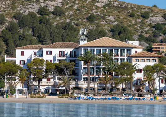 Exterior view of white hotel building with tall palm trees in front of a beach