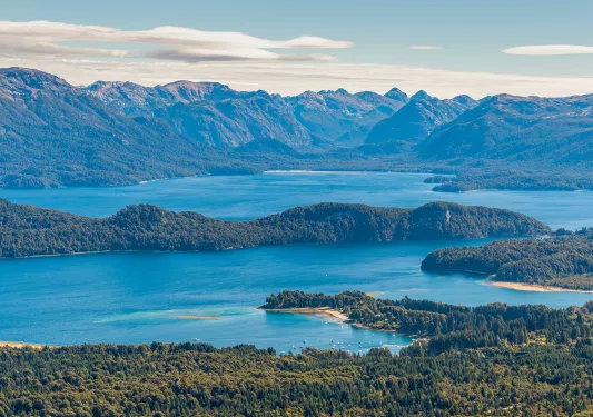 Sky view of a large lake, surrounded by tall mountains and trees
