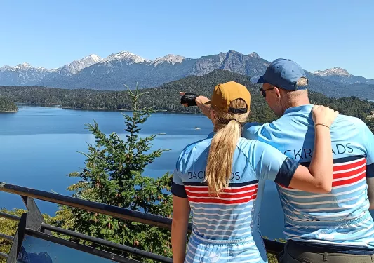 Man and woman wearing blue Backroads jerseys, pointing out towards a lake