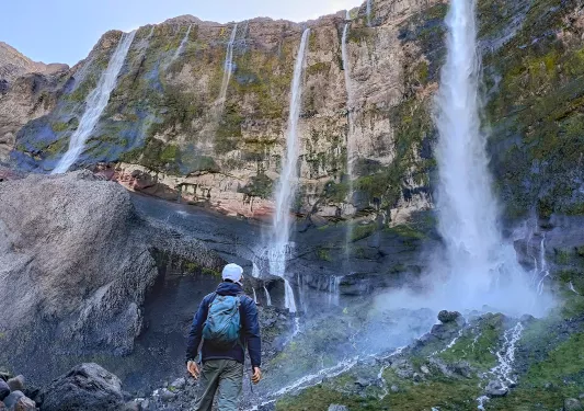 Hiker looking up at a tall cliff with multiple, active waterfalls