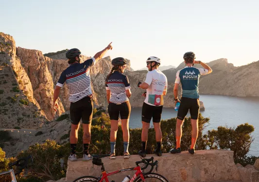 Group of people wearing biking gear, standing on a ledge looking out to a lake