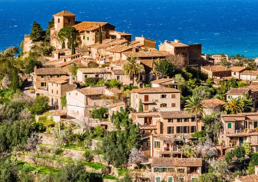 Sky view of a cluster of brown houses on a hill, with the ocean in the background