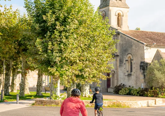 Person in a red jacket riding a bike towards a cathedral