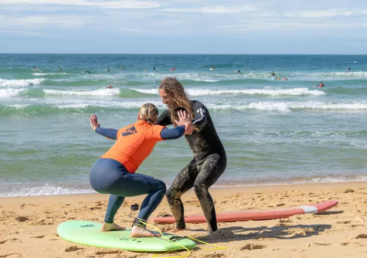 Man and woman practicing surfing on the sand in front of the ocean