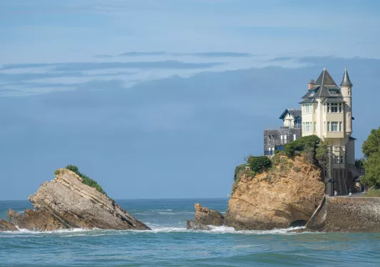 Two large boulders in the ocean with a house on the right