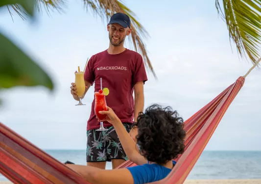 Man standing while raising a glass, with a person sitting on a hammock also raising their glass