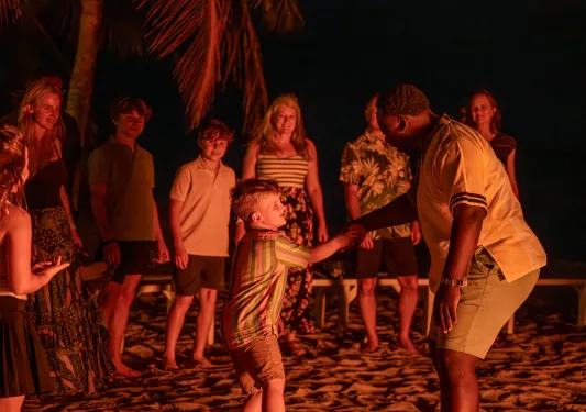 Group of people at a beach bonfire, with a boy and man dancing and smiling