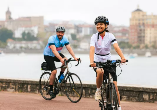 Man and woman riding bikes on a road next to a lake