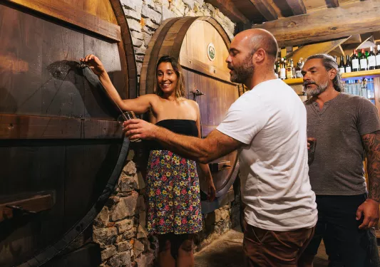 Man and woman pouring alcohol from a barrel in a cellar