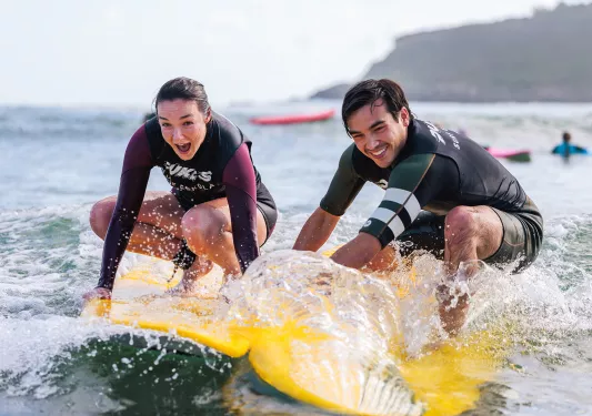 Man and woman standing on yellow surfboards in the ocean
