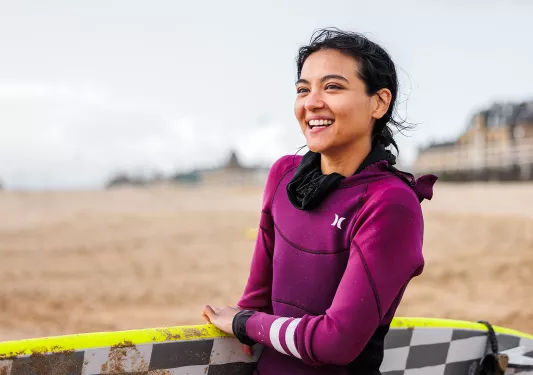 Woman holding a surfboard, smiling on the beach
