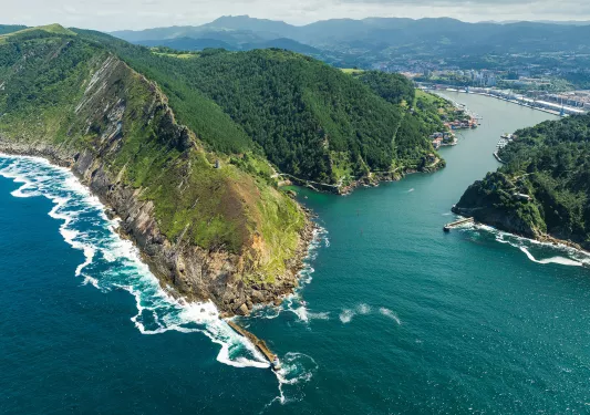Sky view of large hills covered in trees, with the ocean surrounding