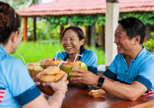 Man and woman smiling while holding up coconuts with straws
