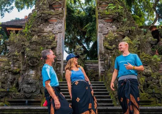 Two men and one women wearing traditional gowns in front of temple ruins