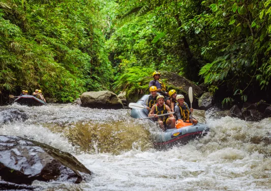 Group of people smiling while paddling on a raft through a river