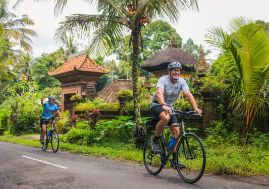 Man and woman biking on a road with jungle in the background