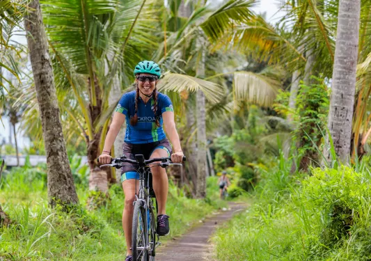 Woman smiling while riding a bike through a road surrounded by palm trees