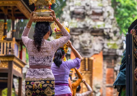 Group of women wearing traditional clothing, holding up small statues on their heads