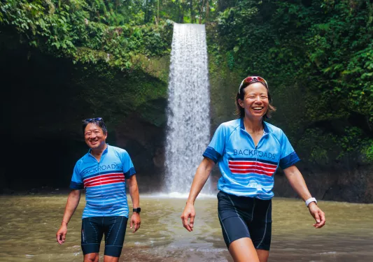 Man and woman walking through a pond in front of a waterfall