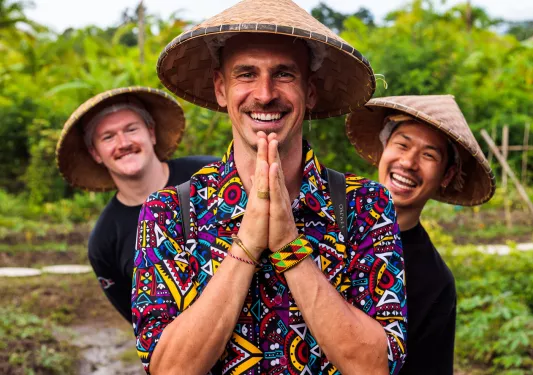 Three men wearing straw hats, smiling in front of a jungle