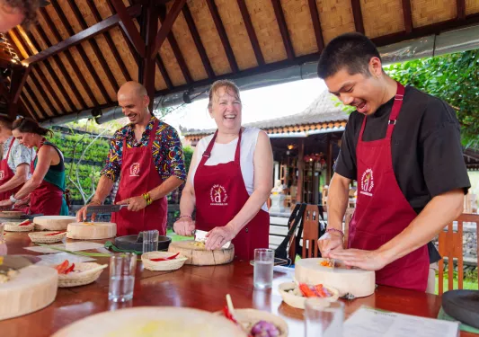 Group of people smiling while chopping vegetables on a wooden plank