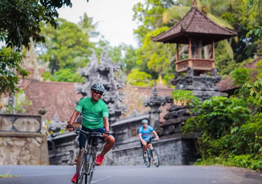 Man smiling while riding a bike on a road, with a temple in the background