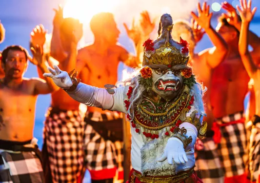Person in traditional attire dancing, while a group of men behind them are dancing