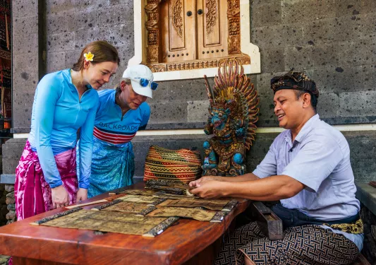 Two women looking at a man making traditional art