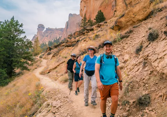 Group of men and women hiking on a dirt trail with large mountains in the background