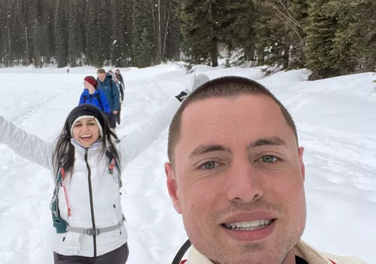 Man and woman smiling, while trekking through a field of snow