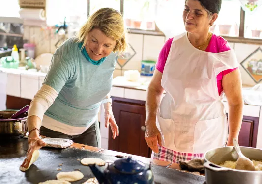 Two women wearing aprons, putting dough onto a hot skillet
