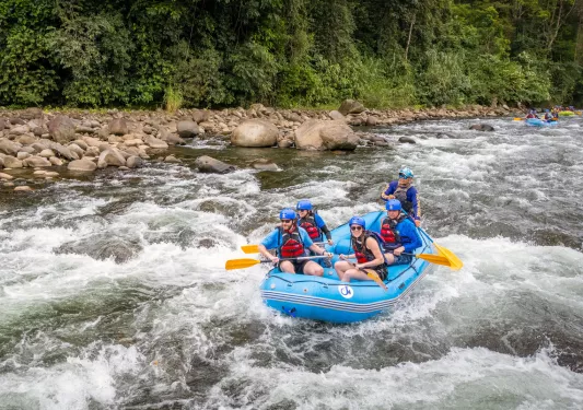 Group of people paddling in a blue raft in an active river